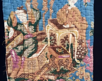 May include: A vintage fabric panel with a quilted blue background featuring a scene of two figures in traditional clothing sitting at a table with a floral design. The fabric is decorated with intricate details and a variety of colors, including brown, green, pink, and yellow.