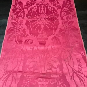 May include: A pink damask fabric with a floral pattern. The fabric has a subtle sheen and a delicate texture.
