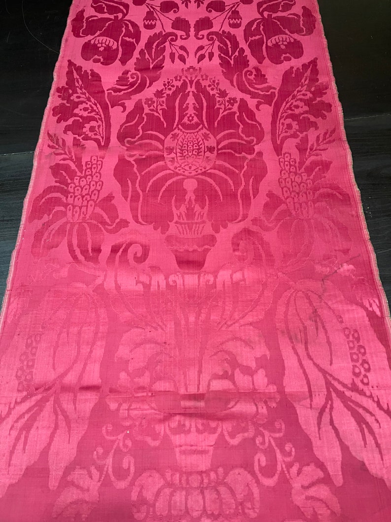 May include: A pink damask fabric with a floral pattern. The fabric has a subtle sheen and a delicate texture.