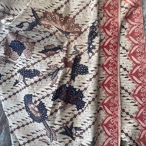 May include: A beige fabric with a brown and black batik pattern. The fabric has a red border with a floral design.