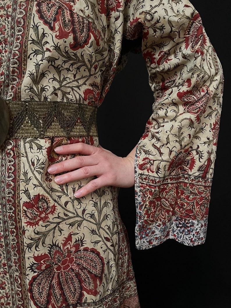 Pu&ograve; includere: Un abito a maniche lunghe color crema con stampa floreale rossa e nera. L'abito ha una cintura con perline e una vita drappeggiata.