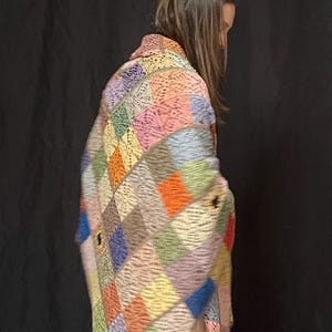 May include: A colorful crocheted blanket with a patchwork design in shades of pink, blue, green, orange, and brown. The blanket is made of squares and has a fringed edge.
