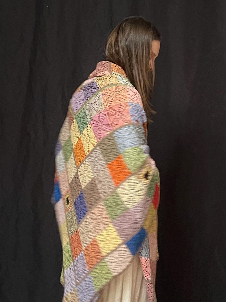 May include: A colorful crocheted blanket with a patchwork design in shades of pink, blue, green, orange, and brown. The blanket is made of squares and has a fringed edge.