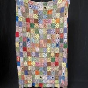 May include: A colorful crocheted blanket with a patchwork design. The blanket is made up of squares of different colors, including red, blue, green, yellow, and pink. The squares are joined together with a white crocheted border.
