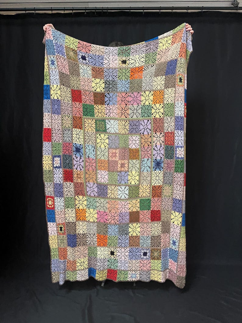 May include: A colorful crocheted blanket with a patchwork design. The blanket is made up of squares of different colors, including red, blue, green, yellow, and pink. The squares are joined together with a white crocheted border.