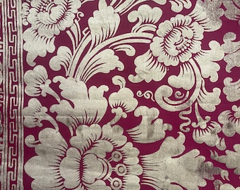 May include: A close-up of a burgundy fabric with a gold floral pattern. The fabric has a repeating pattern of stylized flowers and leaves.