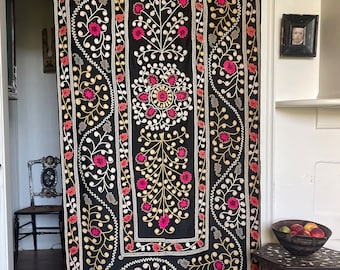 May include: A black fabric wall hanging with intricate embroidery in shades of pink, white, and gold. The design features floral motifs and swirling patterns.