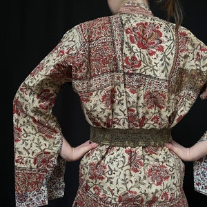 Pu&ograve; includere: Una lunga veste a maniche lunghe di colore crema con stampa floreale rossa e nera. La veste ha una silhouette ampia e fluida e una cintura con una fibbia dorata.