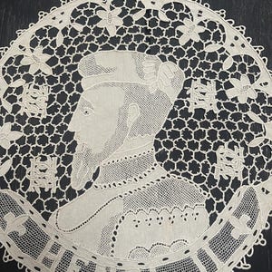 May include: Cream-colored, circular lace doily featuring a portrait of a man, possibly historical, with the name "HENRI" around the border. The lace has a delicate, openwork design with floral and geometric patterns.