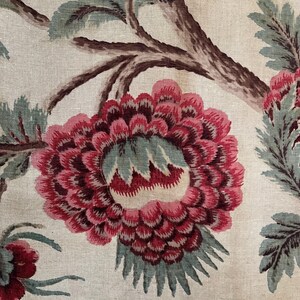May include: A close-up of a floral fabric with a large pink flower with a green center and brown branches. The fabric has a white background.