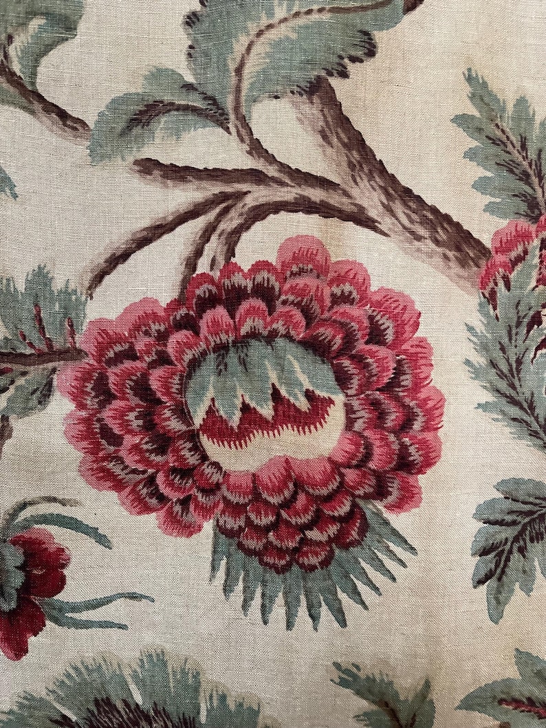 May include: A close-up of a floral fabric with a large pink flower with a green center and brown branches. The fabric has a white background.