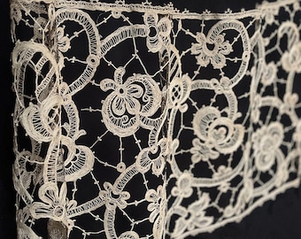 May include: Close-up of a white lace trim with intricate floral patterns against a black background.