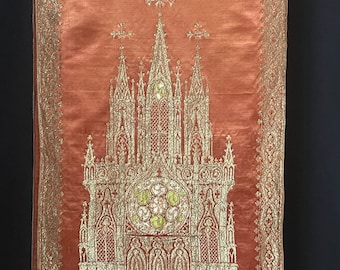 May include: A red fabric wall hanging with a gold embroidered design of a gothic cathedral. The cathedral has a large stained glass window with a circular design in the center.