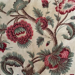 May include: A vintage floral fabric with a repeating pattern of red and green flowers on a cream background. The flowers are stylized and have a slightly faded look.