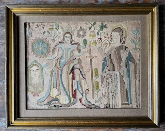 May include: An antique needlepoint sampler with a colorful floral design and two figures in the center. The figures are dressed in elaborate clothing and are surrounded by flowers and leaves. The sampler is framed in a gold frame.