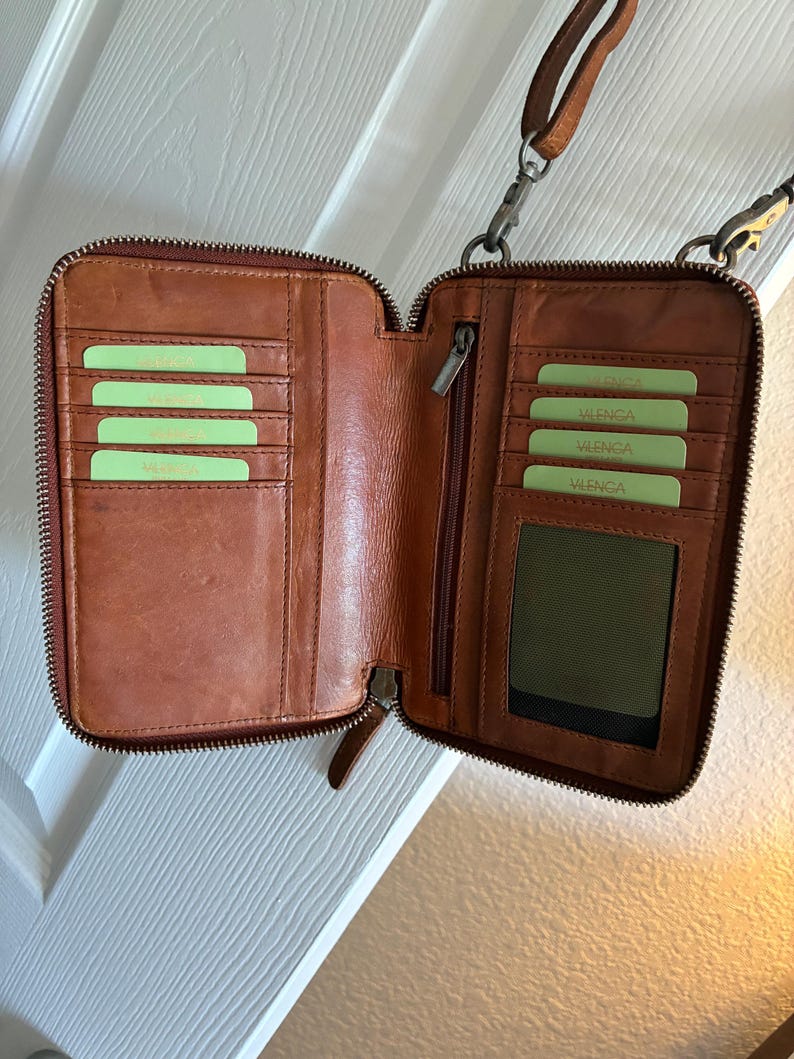Puede incluir: Una cartera de cuero marr&oacute;n con cierre de cremallera, que presenta m&uacute;ltiples ranuras para tarjetas en ambos lados, una ventana transparente para identificaci&oacute;n y un compartimento vertical con cremallera. Incluye una correa extra&iacute;ble con clips.