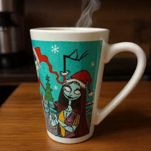 Może przedstawiać: Biały ceramiczny kubek o zwężanym kształcie z turkusowym tłem i grafiką przedstawiającą Sally z Miasteczka Halloween w czapce Mikołaja, z unoszącą się parą oraz białymi akcentami w kształcie płatk&oacute;w śniegu na powierzchni kubka.