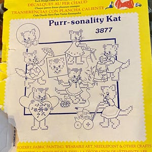 May include: A yellow and white iron-on transfer sheet with a design of seven cats in various poses. The sheet is titled "Purr-sonality Kat" and has the number 3877 printed on it. The text "Hot Iron Transfers" is printed at the top of the sheet.