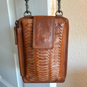 Puede incluir: Un bolso bandolera rectangular de cuero marr&oacute;n con una textura trenzada en el panel frontal, un cierre de solapa central y un compartimento principal con cremallera. Incluye una correa de cuero extra&iacute;ble con clips y herrajes de metal oscuro.
