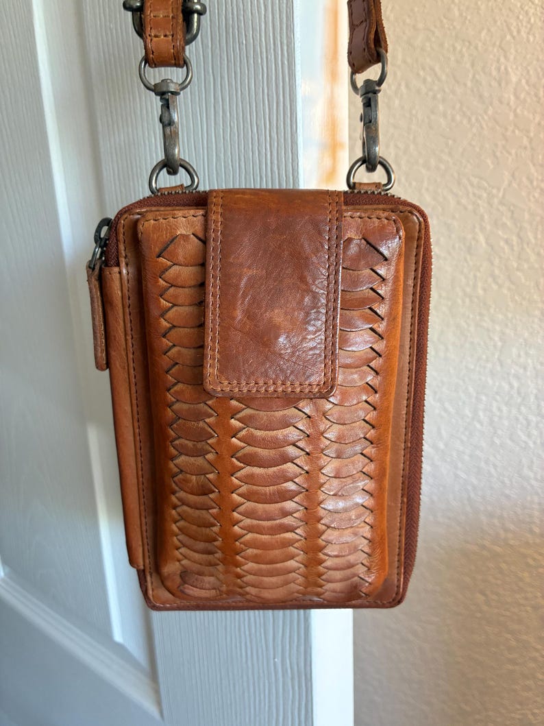 Puede incluir: Un bolso bandolera rectangular de cuero marr&oacute;n con una textura trenzada en el panel frontal, un cierre de solapa central y un compartimento principal con cremallera. Incluye una correa de cuero extra&iacute;ble con clips y herrajes de metal oscuro.