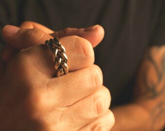 May include: A silver braided ring worn on a person's finger.