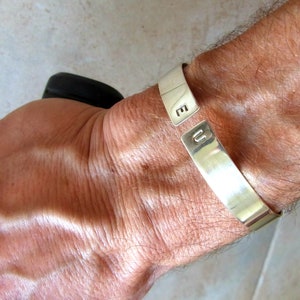 May include: A silver cuff bracelet with the letters "E" and "U" engraved on it.