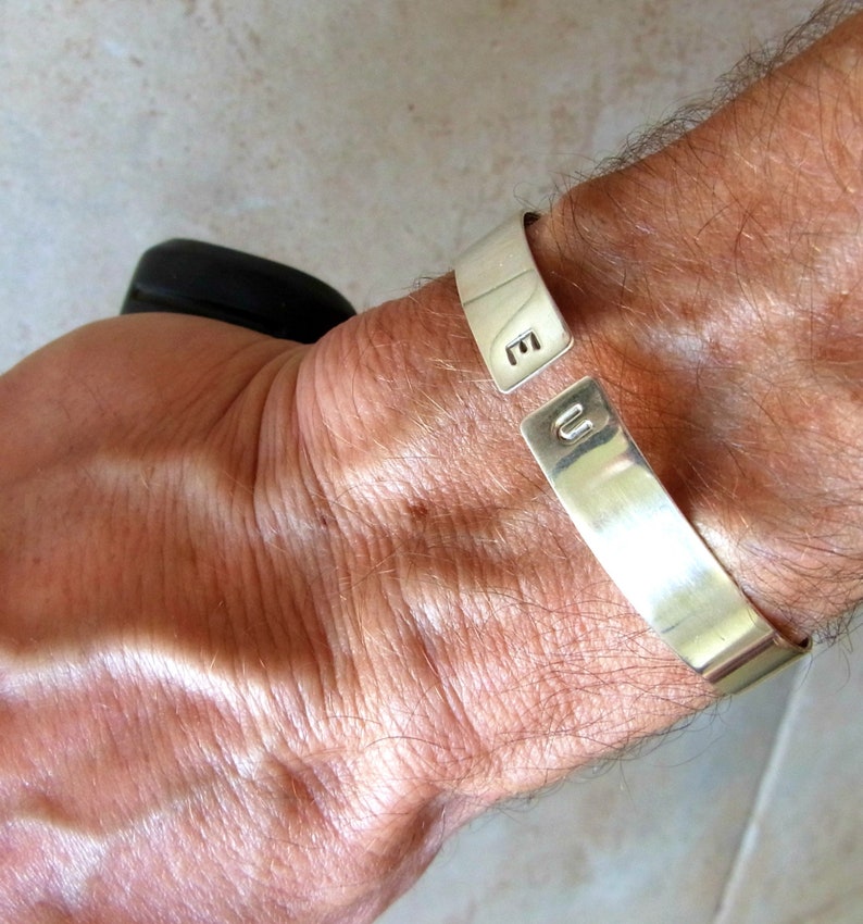 May include: A silver cuff bracelet with the letters "E" and "U" engraved on it.
