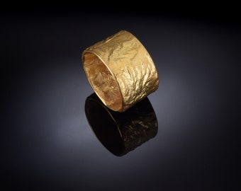 May include: A wide gold band ring with a textured surface. The ring is made of metal and has a hammered finish.