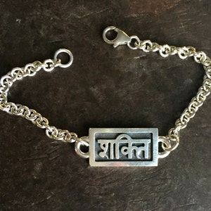 May include: A silver bracelet with a rectangular charm that says "शांति" in Hindi script.