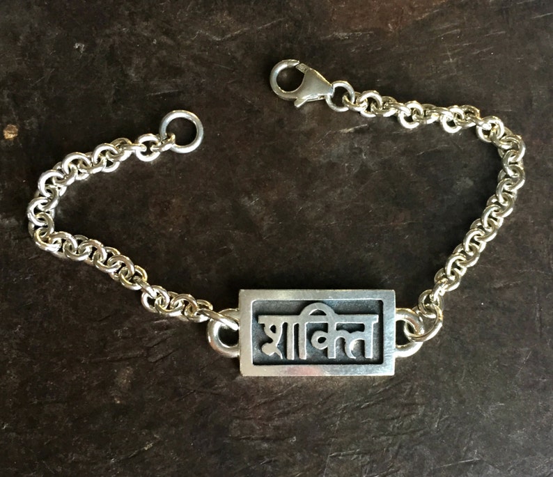 May include: A silver bracelet with a rectangular charm that says "शांति" in Hindi script.