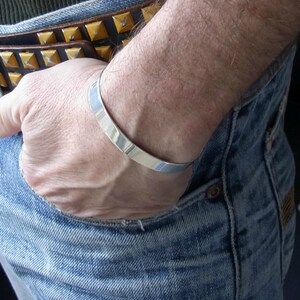 May include: A silver bangle bracelet worn on a person's wrist. The bracelet is simple and sleek, with a polished finish.