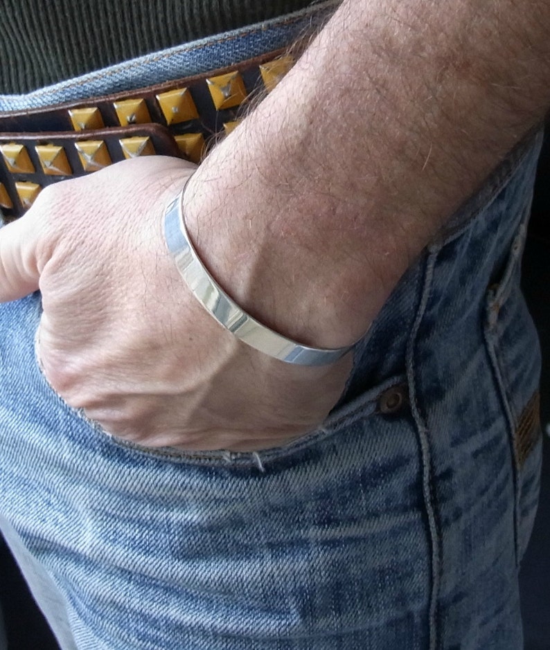May include: A silver bangle bracelet worn on a person's wrist. The bracelet is simple and sleek, with a polished finish.