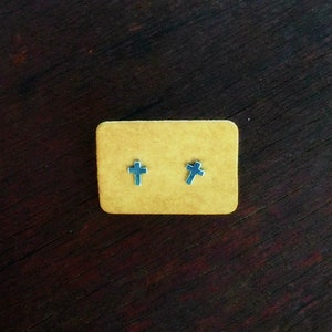 May include: Two silver cross stud earrings displayed on a brown card.