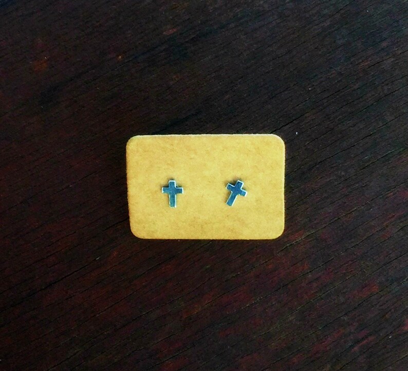 May include: Two silver cross stud earrings displayed on a brown card.