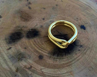 May include: A gold ring with a knotted design. The ring is made of a thick, smooth metal and has a simple, modern style.