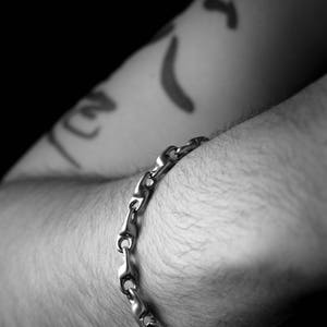 K&ouml;nnte beinhalten: Ein silbernes Kettenarmband am Arm einer Person. Das Armband besteht aus ineinandergreifenden Gliedern.