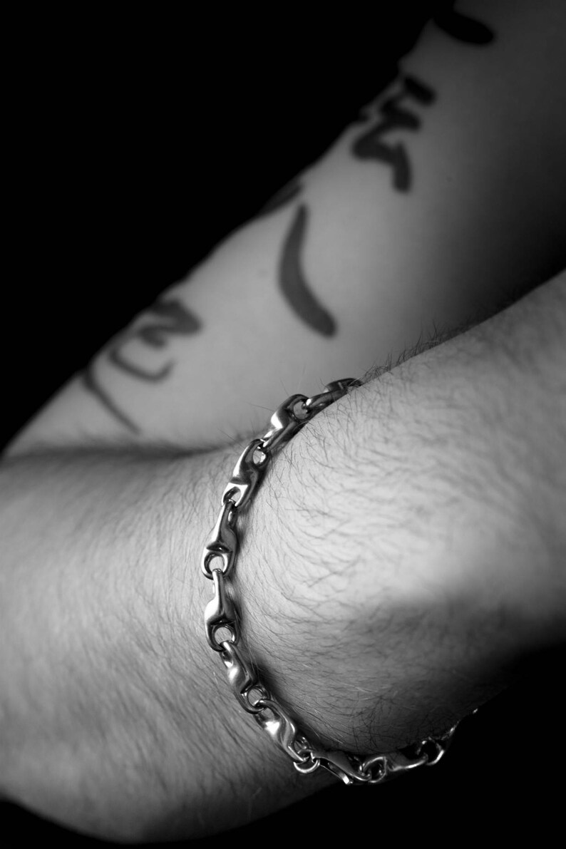 K&ouml;nnte beinhalten: Ein silbernes Kettenarmband am Arm einer Person. Das Armband besteht aus ineinandergreifenden Gliedern.