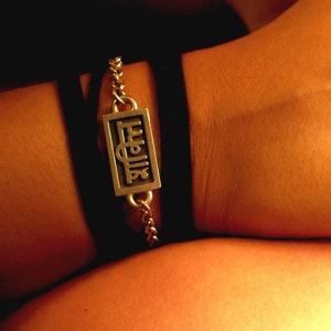 May include: A silver bracelet with a rectangular charm that says "Fuelia" in a stylized font. The bracelet is worn on a person's wrist.