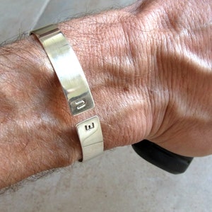 May include: A silver cuff bracelet with the letters "U" and "E" engraved on the front.