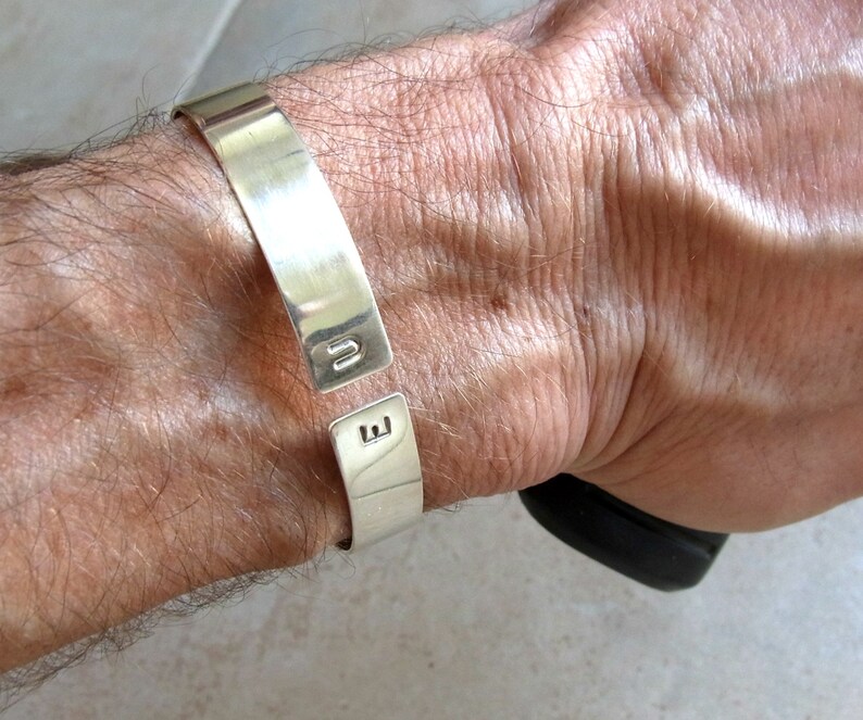 May include: A silver cuff bracelet with the letters "U" and "E" engraved on the front.