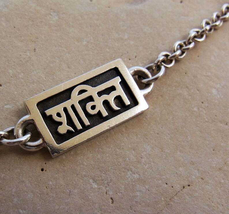 May include: Silver chain necklace with a rectangular pendant featuring the word "शक्ति" in Hindi script.