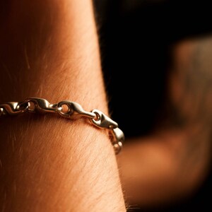 K&ouml;nnte beinhalten: Ein silbernes Kettenarmband mit einem Gliederdesign. Das Armband wird am Handgelenk getragen.