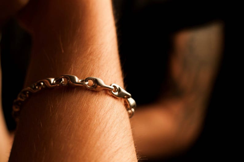 K&ouml;nnte beinhalten: Ein silbernes Kettenarmband mit einem Gliederdesign. Das Armband wird am Handgelenk getragen.
