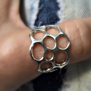 May include: A silver ring with a honeycomb-like design. The ring is made of a series of interconnected circles.