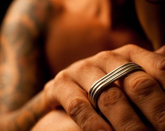 May include: A silver ring with a multi-layered design. The ring is worn on the index finger of a person's hand.