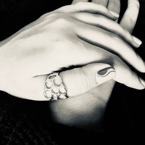 May include: A silver ring with a honeycomb design. The ring is worn on the thumb of a hand with a black and white nail design.