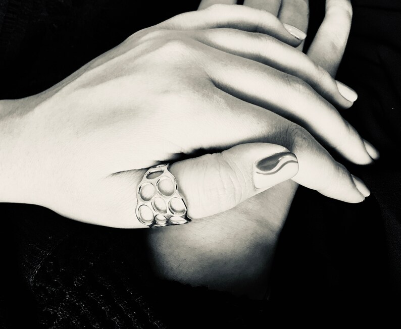 May include: A silver ring with a honeycomb design. The ring is worn on the thumb of a hand with a black and white nail design.