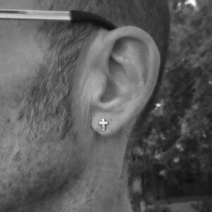 May include: A close-up of a person's ear with a small silver cross earring.