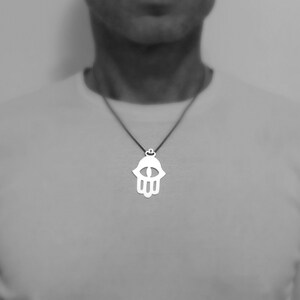 May include: A silver necklace with a hamsa hand pendant featuring an eye in the center.