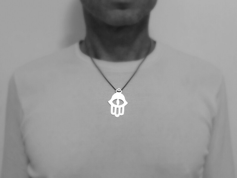 May include: A silver necklace with a hamsa hand pendant featuring an eye in the center.